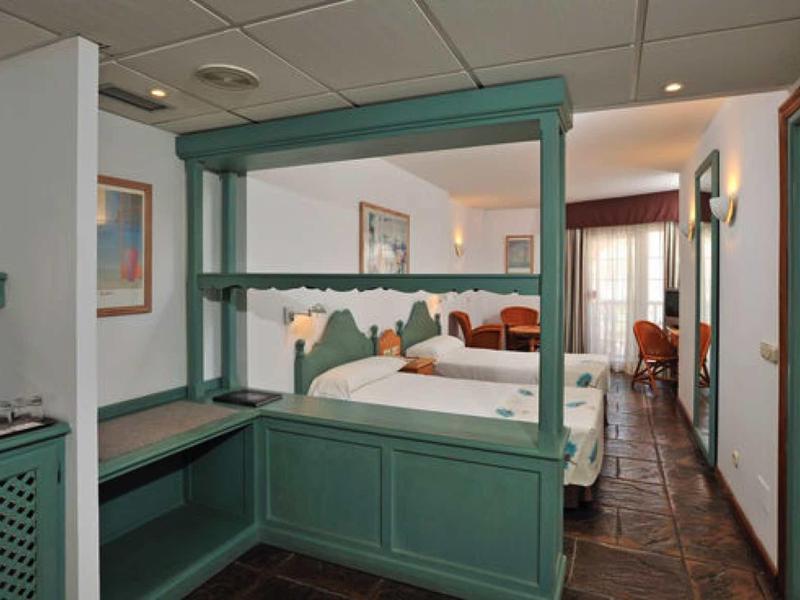 Hotelzimmer mit grünem Holzbalken, Doppelbett, Bad und Fliesenboden, hell und freundlich gestaltet.