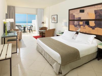 Hell eingerichtetes Hotelzimmer mit großem Bett, Balkon und Meerblick, moderner Dekoration.