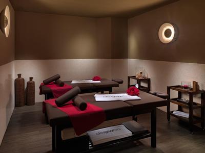 Ein ruhiger Massageraum mit zwei Massageliegen, braunen Wänden und roter Dekoration.