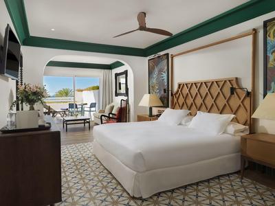 Modernes Hotelzimmer mit großem Bett, Ventilator, Sitzbereich und Blick auf Terrasse.