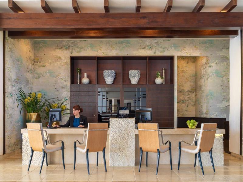 Moderner Essbereich mit sechs beigen Stühlen um Tisch, Betonwand und Holzdecke mit sichtbaren Balken.