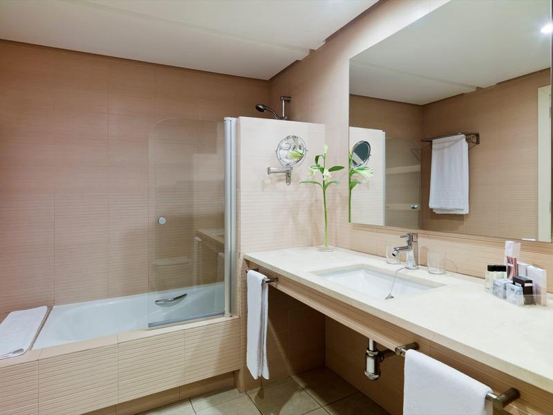 Moderne Badezimmer mit Badewanne, großem Spiegel und Waschbecken auf cremefarbenem Waschtisch.