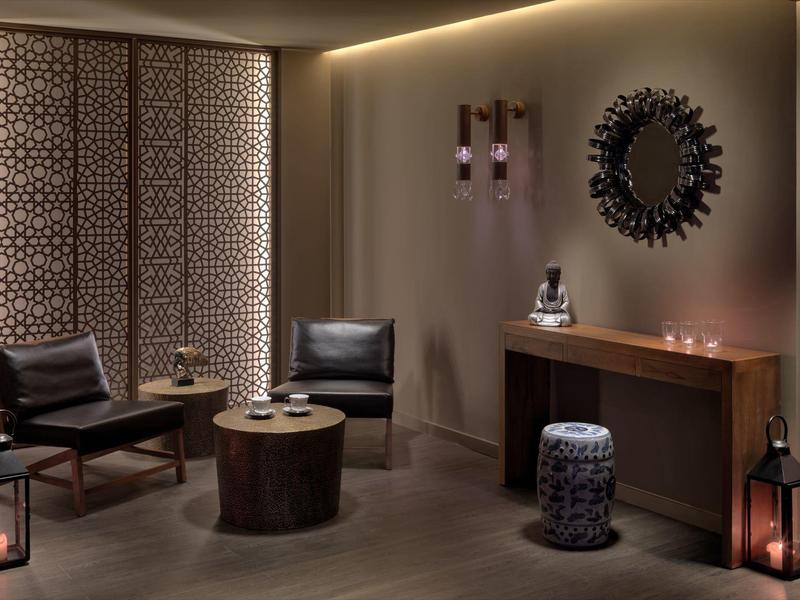 Elegantes Wohnzimmer mit dunklen Sesseln, Holzkommode, rundem Teppich und dekorativem Wandspiegel.