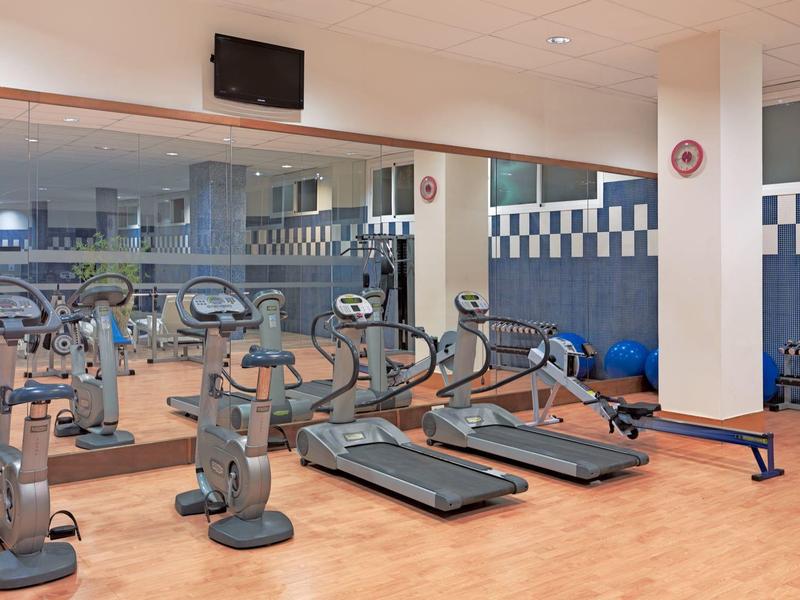 Moderner Fitnessraum mit Laufbändern, Fahrrädern, Rudergerät und Trainingsbank auf Holzboden.