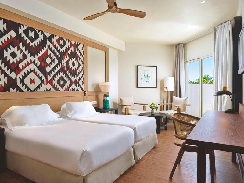 Hell eingerichtetes Hotelzimmer mit zwei Einzelbetten und Fenster mit Blick ins Grüne.