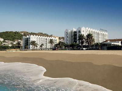 Großes Hotel am Strand mit sanften Wellen und klarem Himmel im Hintergrund.
