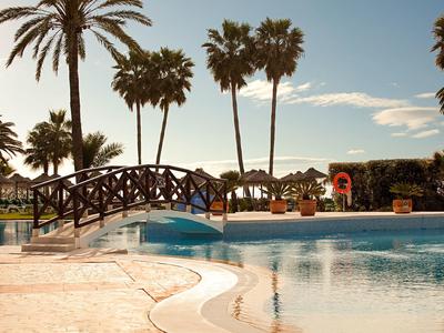 Pool mit einer kleinen Brücke und Palmen im Hintergrund bei Sonnenuntergang