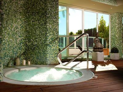 Innenraum mit Whirlpool, Mosaikwänden und Panorama-Fenstern, Sonnenlicht fällt herein.