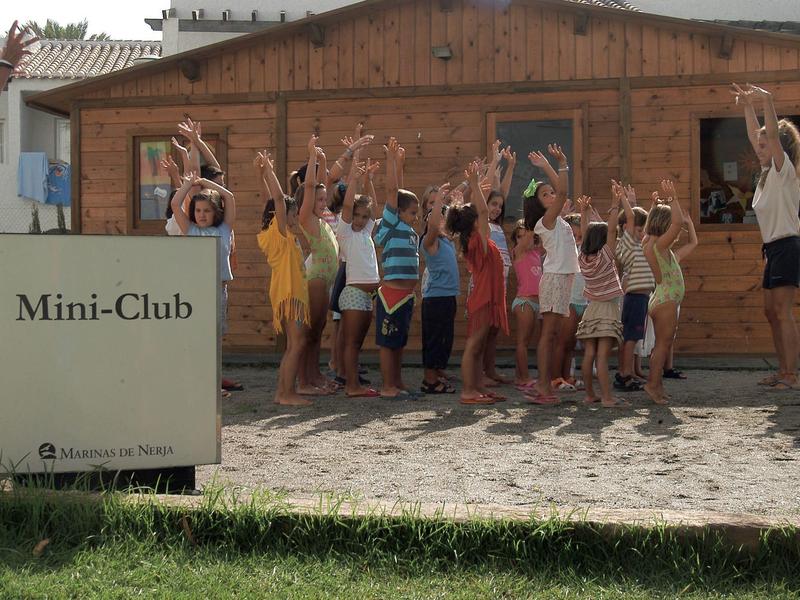 Kindergruppe macht gemeinsam Übungen vor einem Holzgebäude im Mini-Club.