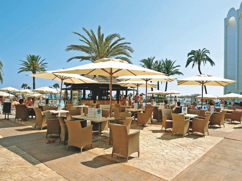 Freiluftrestaurant mit vielen Tischen und Sonnenschirmen an einem sonnigen Tag.