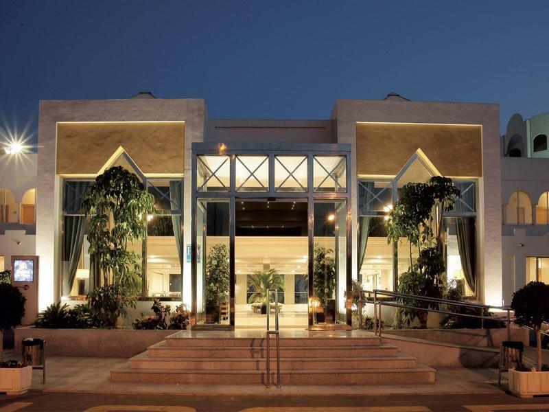 Elegantes Hotelgebäude bei Nacht mit beleuchtetem Eingang und Palmen