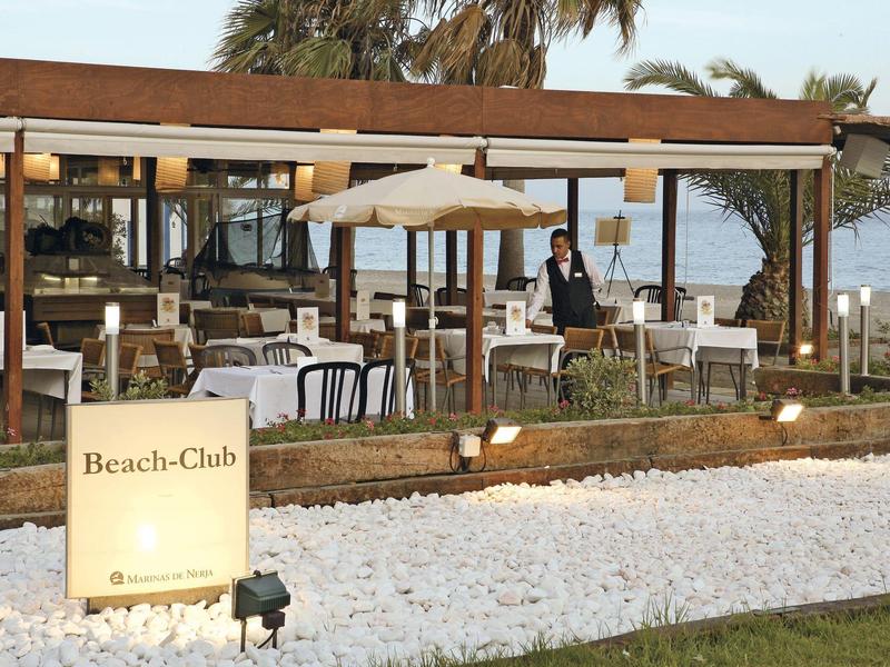 Strandclub mit gedeckten Tischen, Sonnenschirm und einem Kellner am Meer
