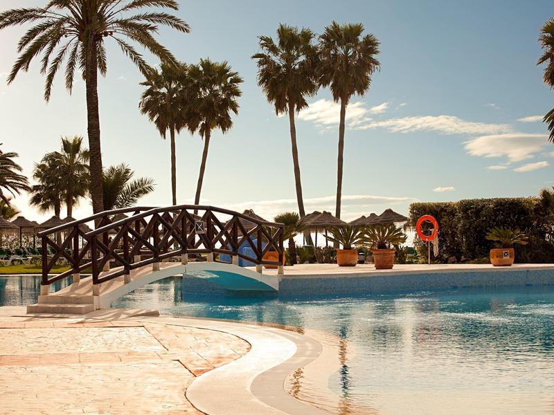 Pool mit einer kleinen Brücke und Palmen im Hintergrund bei Sonnenuntergang
