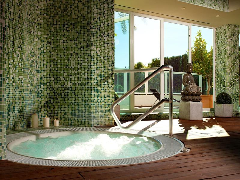 Innenraum mit Whirlpool, Mosaikwänden und Panorama-Fenstern, Sonnenlicht fällt herein.