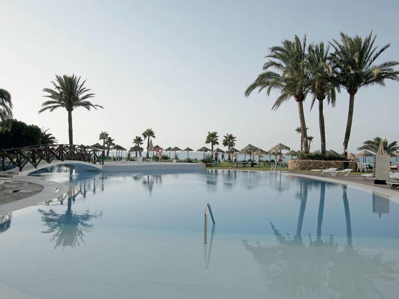 Großer Pool mit Palmen und Liegestühlen in einem sonnigen Hotelresort