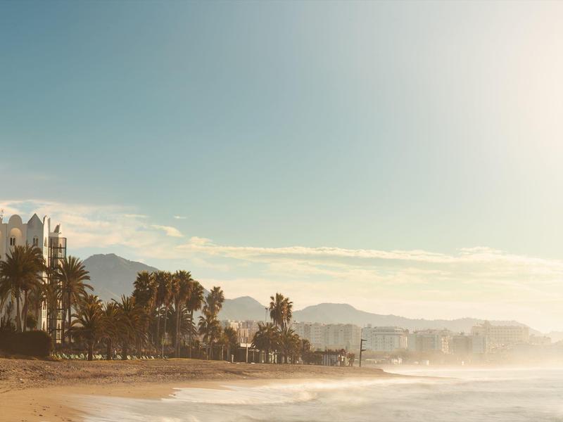 Strand mit Palmen, Wolken und Bergen im Hintergrund bei Sonnenaufgang oder Sonnenuntergang