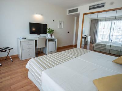 Helles Hotelzimmer mit Doppelbett, TV an der Wand, Schreibtisch, Stuhl und großem Spiegel.