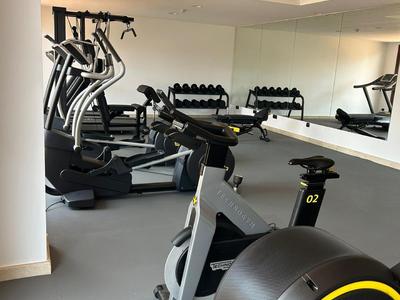 Fitnessraum mit Trainingsgeräten wie Fahrradergometer, Crosstrainer und Hanteln vor großem Spiegel.
