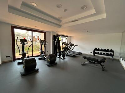 Fitnessraum mit mehreren Trainingsgeräten, Hanteln und großen Fenstern mit Gartenblick.
