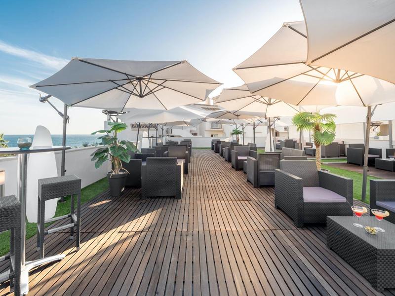 Dachterrasse mit Holzboden, schwarzen Loungemöbeln und weißen Sonnenschirmen bei Tageslicht.