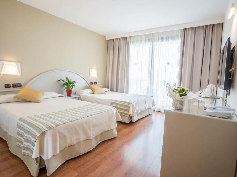 Hell eingerichtetes Hotelzimmer mit zwei großen Betten, Balkon und modernem Mobiliar.