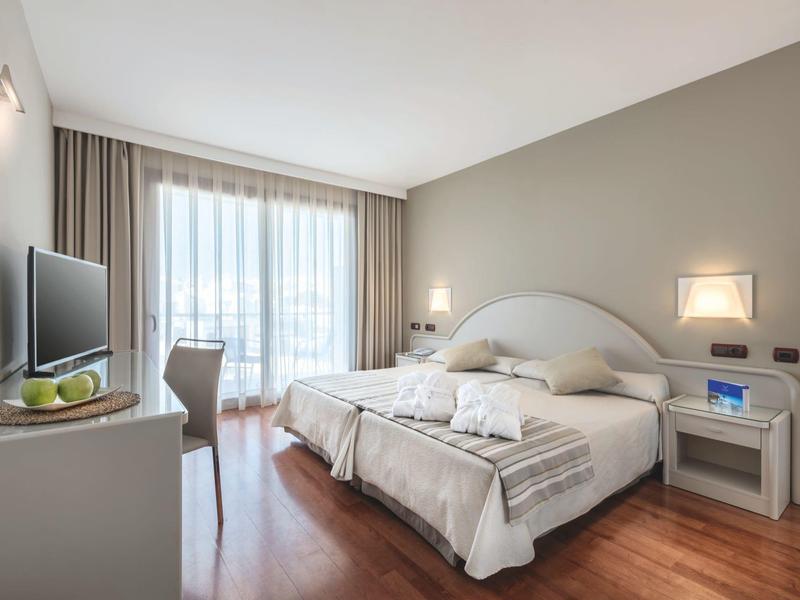 Helles, modernes Schlafzimmer mit Doppelbett, Holzfußboden, TV und großem Fenster mit Gardinen.