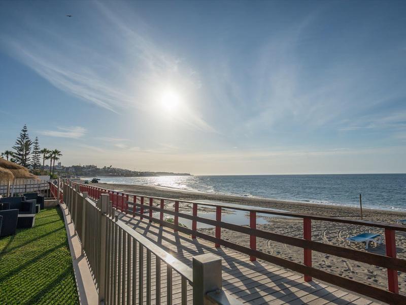 Sonnenuntergang am Strand mit Holzzaun, grüner Wiese und blauem Himmel mit leichten Wolken.