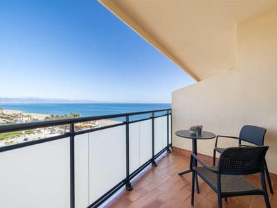 Balcony with table and two chairs overlooking the sea and sky on a sunny day.