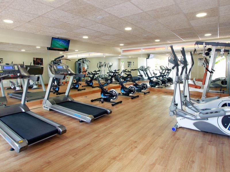 Moderner Fitnessraum mit Laufbändern, Crosstrainern und Spiegelwand, helle Holzfußbodenfläche.