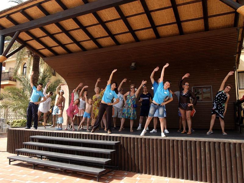 Modernes Wohnzimmer mit grauem Sofa, Holztisch, Wanddeko aus Blättern und Balkon im Hintergrund.