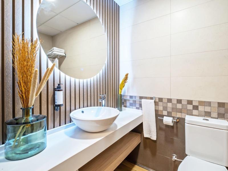 Modernes Badezimmer mit rundem Spiegel, Waschbecken auf Holzplatte und weißen Fliesen.