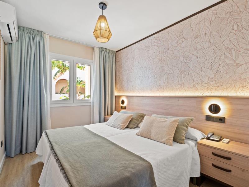 Modernes Schlafzimmer mit Doppelbett, hellem Holz, gedämpfter Beleuchtung und großen Fenstern.