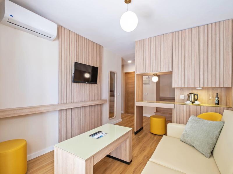 Gemütliches Wohn- und Küchenzimmer mit hellem Holz, gelben Akzenten und moderner Beleuchtung.