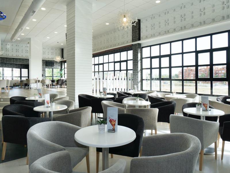 Modernes Café mit großen Fenstern, weißen Tischen und grauen sowie schwarzen Sesseln.