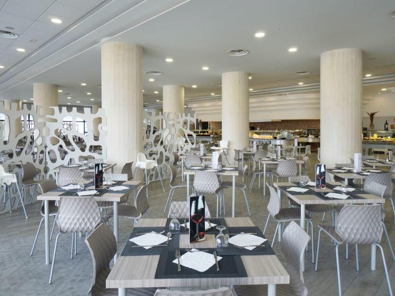 Großer, moderner Speisesaal mit weißen Stühlen, runden Tischen, grauem Boden und Säulen im Raum.