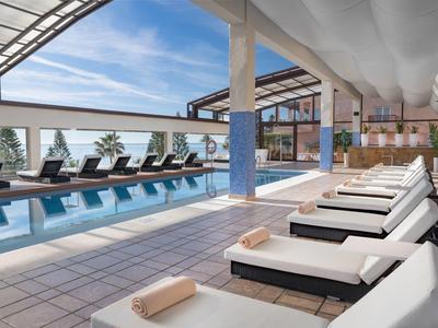 Modernes Hallenbad mit Liegestühlen, großen Fenstern und hellem Fliesenboden.