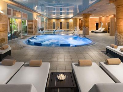 Eleganter Wellnessbereich mit Whirlpool, Liegen, warmem Licht und großer Fensterfront.