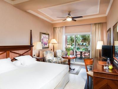 Hell eingerichtetes Hotelzimmer mit großem Bett, Sitzbereich, Schreibtisch und Balkon mit Sicht ins Grüne.