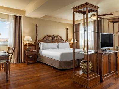 Helles, elegantes Hotelzimmer mit Holzboden, großem Bett, Schreibtisch, Stehlampen und TV-Möbel.