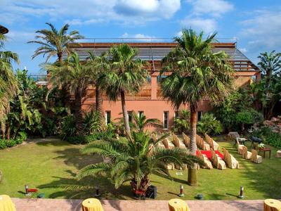 Ein tropischer Garten mit Palmen und einer großen, roten Hotelanlage im Hintergrund.