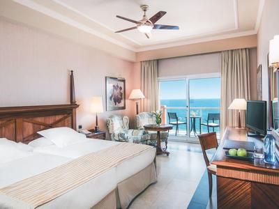 Helles Hotelzimmer mit Doppelbett, Meerblick und Balkon mit Sitzgelegenheit.