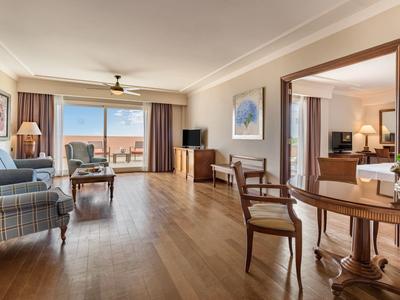 Geräumiges Wohnzimmer mit Holzboden, Sesseln, Tisch, Fernseher und großem Fenster mit Meeresblick.