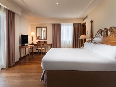 Hell eingerichtetes Schlafzimmer mit großem Bett, Holzfußboden, Fenster und Schreibtisch.