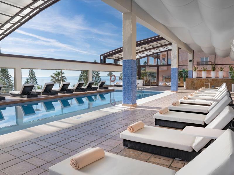 Modernes Hallenbad mit Liegestühlen, großen Fenstern und hellem Fliesenboden.