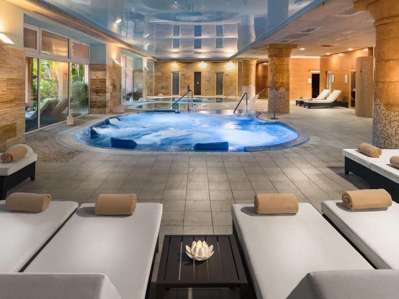 Eleganter Wellnessbereich mit Whirlpool, Liegen, warmem Licht und großer Fensterfront.