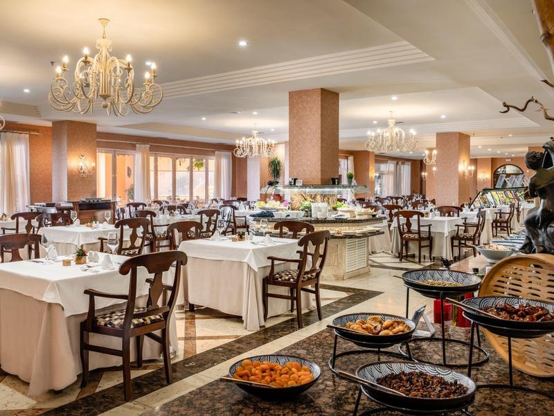 Elegantes Restaurant mit gedeckten Tischen, Holzstühlen und Kronleuchtern in warmem Licht.