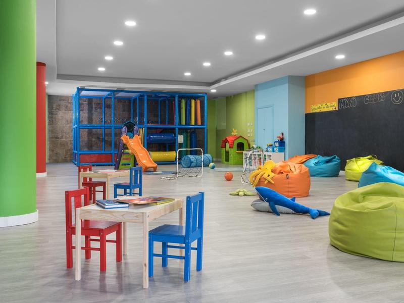 Kinderspielzimmer mit bunten Möbeln, Rutsche, Sitzsäcken und Spielgeräten, helle Beleuchtung.