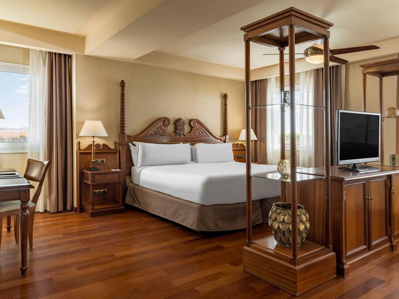 Helles, elegantes Hotelzimmer mit Holzboden, großem Bett, Schreibtisch, Stehlampen und TV-Möbel.