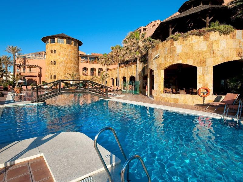 Hotelpool mit mediterranem Stil, blauem Wasser und sonnigem Himmel.