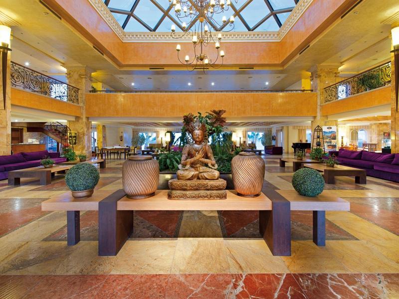 Eleganter Hotellobby mit Dekoration und Glasdach, warme Beleuchtung.